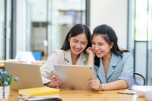Happy two Asian business woman discuss investment project working and planning strategy on digital tablet. Business people talking together with tablet at office. © amnaj