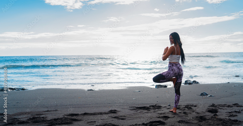 woman in sport clothes practicing yoga and meditating on beach in morning