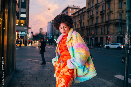 Young stylish black curly woman posing outdoor looking over smiling shy and bashful photo