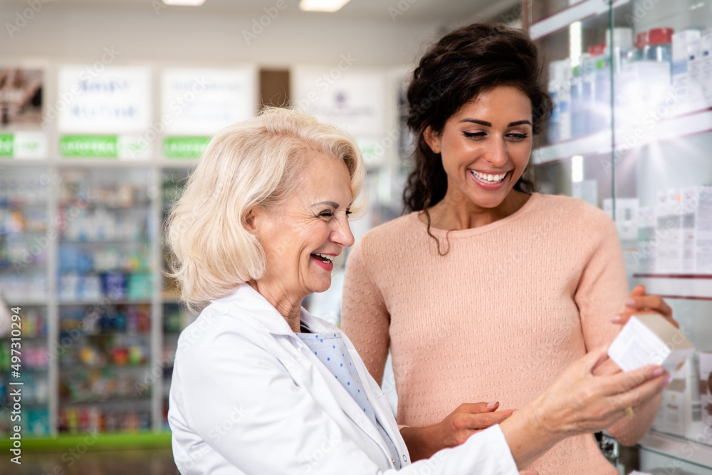 Senior pharmacist selling medications to young female customer in the pharmacy store.