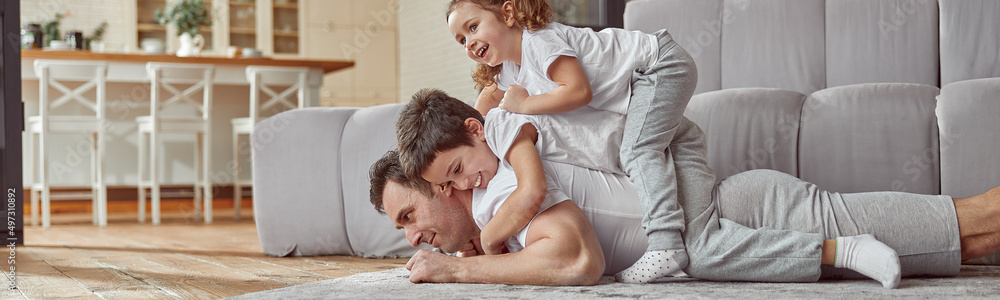 Low angle of jolly son and daughter on dad back while he is lying on floor during training at home Low angle of jolly son and daughter on dad back while he is lying on floor during training at home