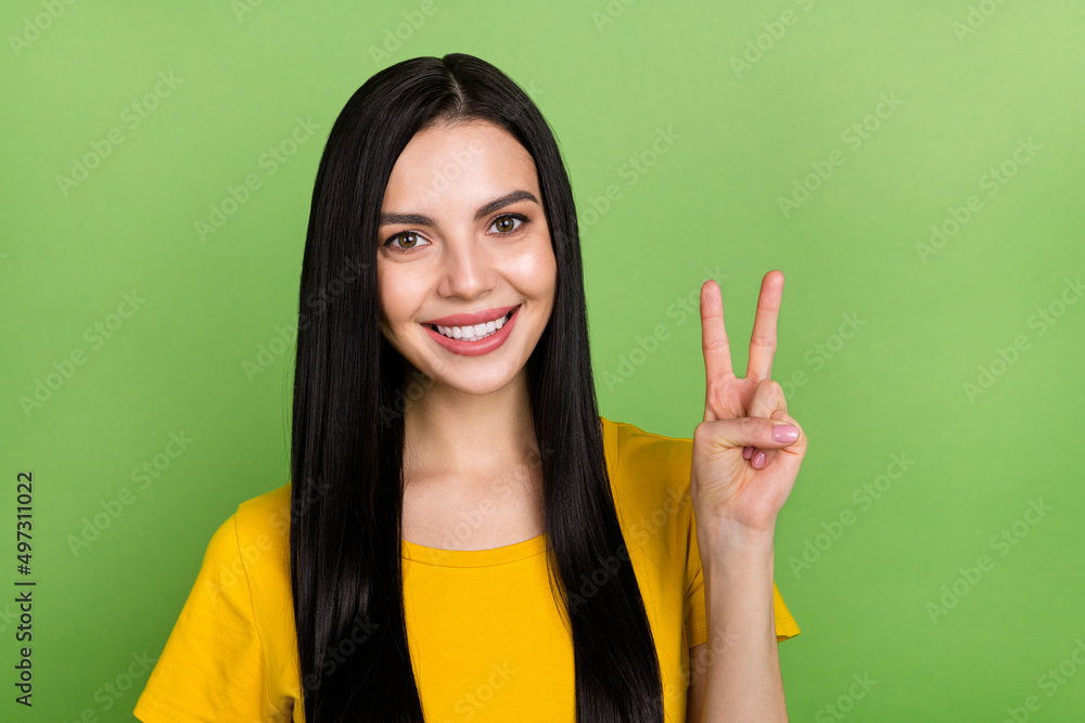 Photo of charming shiny lady dressed yellow t-shirt showing v-sign gesture isolated green color background Photo of charming shiny lady dressed yellow t-shirt showing v-sign gesture isolated green color background