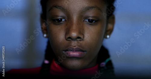 African teen girl browsing online in front of laptop screen, close-up portrait face