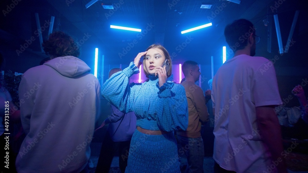A cute girl is anxiously talking on the phone, a crowd of people are dancing around the girl on the dance floor of a nightclub under the light of colored spotlights. Night club A cute girl is anxiously talking on the phone, a crowd of people are dancing around the girl on the dance floor of a nightclub under the light of colored spotlights. Night club