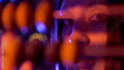 Close-up of a girl counting on old wooden accounts under neon light. Night club. Beautiful compositions with people in neon light. A model girl poses for the camera under a neon light.