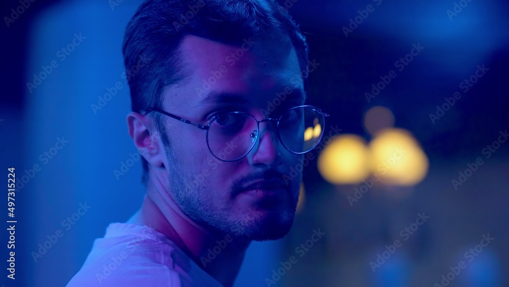 Close-up of a young man looking into the camera under a neon light. Night club