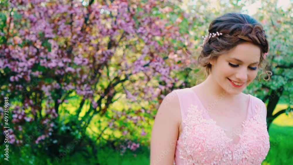 Cute happy adult girl princess with smile on face walks in spring blooming garden. Background park green trees, white pink flowers. Woman is joyful, cheerful, funny, emotional portrait. elegant dress