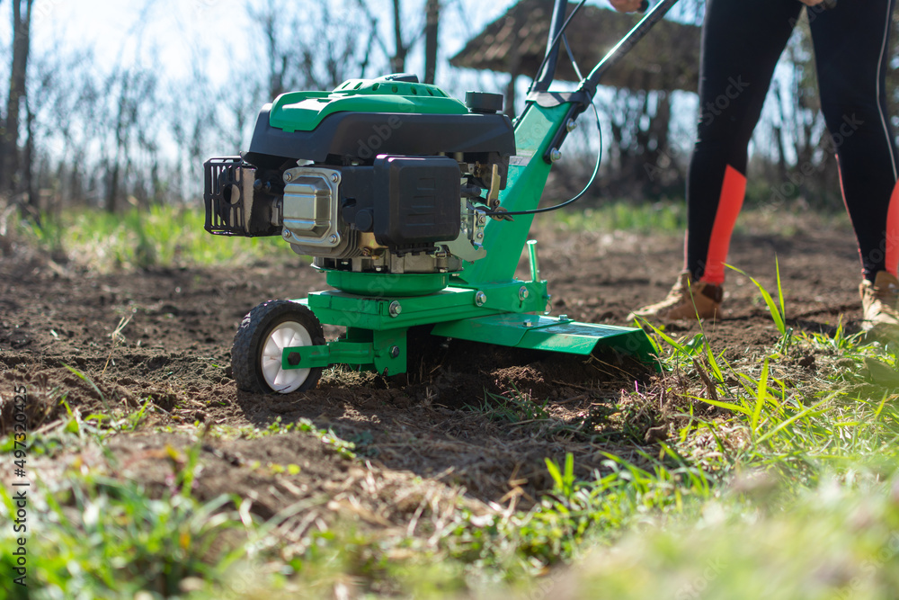 Obraz premium close up photo of female farmer gardener cultivate ground soil rototiller , tiller tractor, cultivator, milling machine, prepare for planting crop, spring. modern farming, technology agriculture