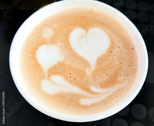 Top view of a paper cup of coffee with foam in the shape of hearts.