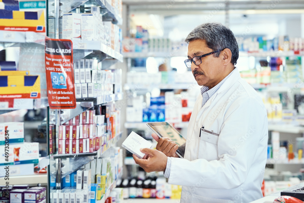 Managing medical matters in his pharmacy. Shot of a mature pharmacist using a digital tablet while working in a chemist.