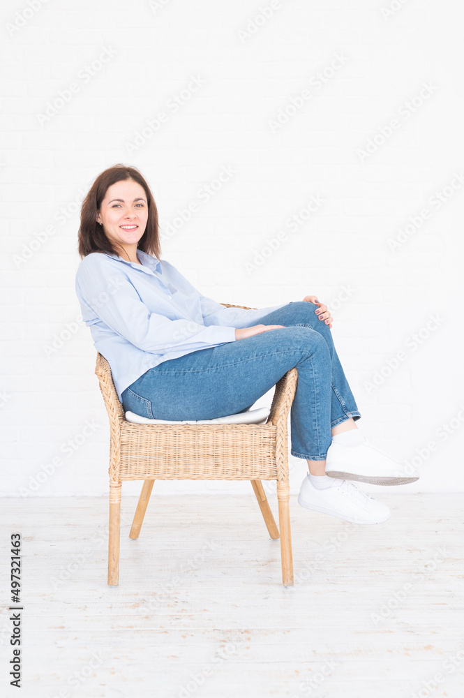 Pretty plus size model woman in shirt and jeans posing in studio on chair, white background with copy space Pretty plus size model woman in shirt and jeans posing in studio on chair, white background with copy space