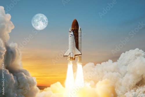 Fototapeta Naklejka Na Ścianę i Meble -  Spaceship lift off. Space shuttle with smoke and blast takes off into space on a background of a sunset with a full moon in the sky. Elements of this image furnished by NASA.