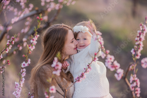 Mother and little daughter are having fun in the blooming rose gardens. Portrait woman hugging girl