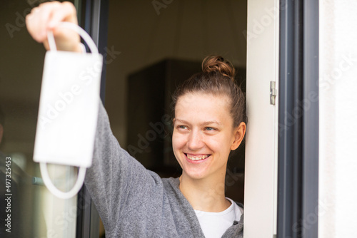 Junge Frau mit blonden Haaren, Dutt, wirft Mundschutzmaske weg aus dem Fenster