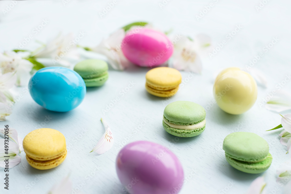 Obraz premium Delicate Easter background of white flowers, petals of colored macaroons and colored eggs. Spring gentle background. 