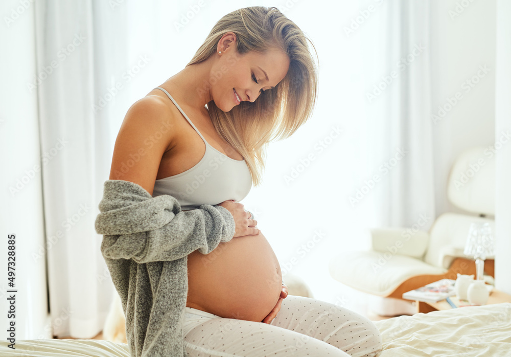 I cant wait to hold you in my arms. Shot of a pregnant woman touching her belly while sitting on her bed. - obrazy, fototapety, plakaty 