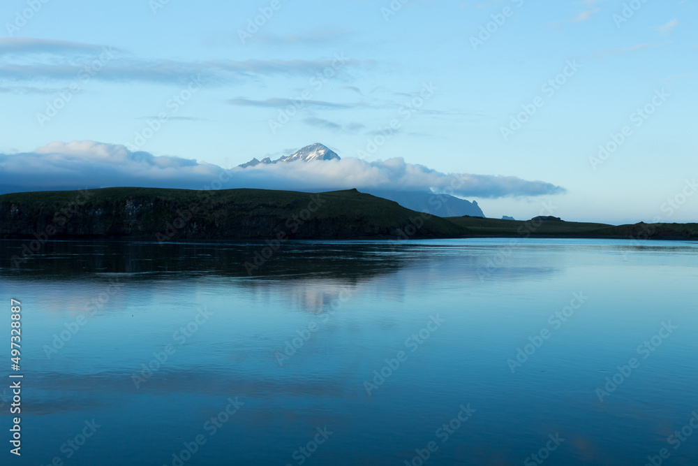 Fototapeta premium Mountains with low clouds seen across a fjord during a late evening blue hour with mountains in soft focus, Hofn, Iceland