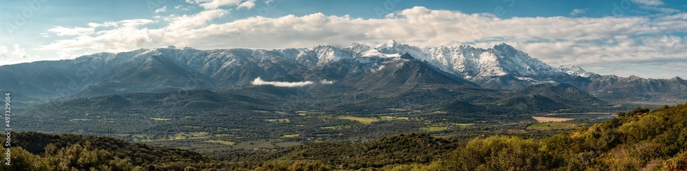 Panoramic view of the Regino valley and Lac de Codole in the Balagne region of Corsica with the snow capped peaks of Monte Padru, Monte San Parteo and Monte Grosso in the distance