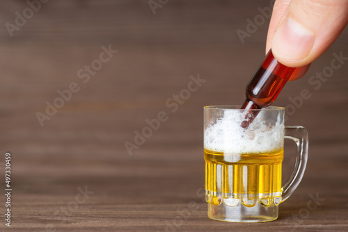 Pouring beer from a tiny bottle into a small beer mug standing on a wooden table. Moderate alcohol consumption concept.