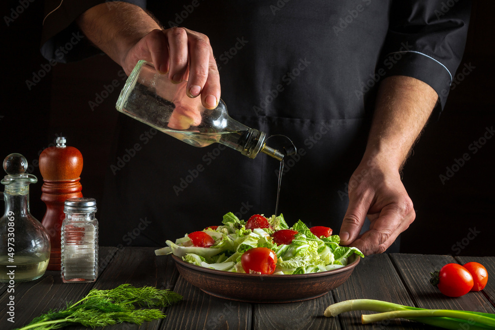 The chef pours oil into salad bowl in the kitchen. Cooking delicious and healthy food with a set of vitamins
