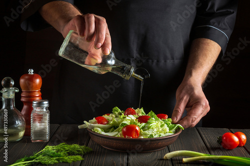 Fototapeta Naklejka Na Ścianę i Meble -  The chef pours oil into salad bowl in the kitchen. Cooking delicious and healthy food with a set of vitamins