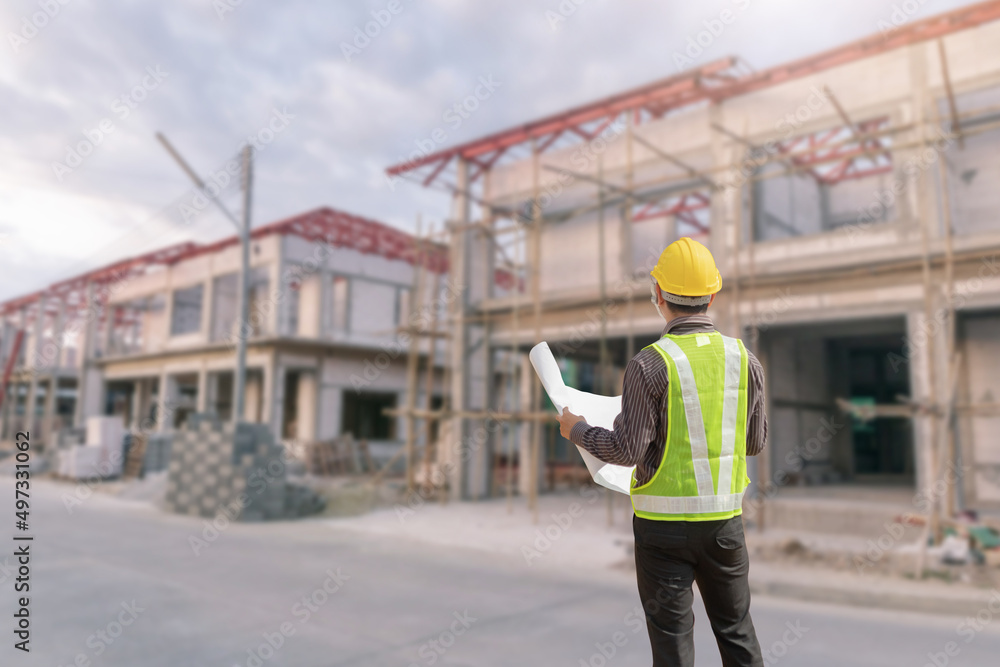 young professional engineer in protective helmet and blueprints paper at the house building construction site young professional engineer in protective helmet and blueprints paper at the house building construction site