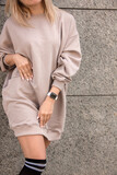 shopping leisure. closeup clothes design details. blonde girl in beige oversize dress stands casual with hands near waist on the modern store background. lifestyle concept, free space