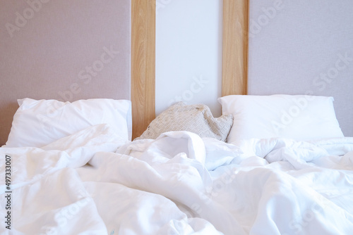 Front face view of unmade bed, white pillows and blankets on bed sheet