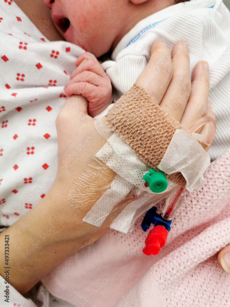Woman holding her newborn baby with peripheral venous catheter on her