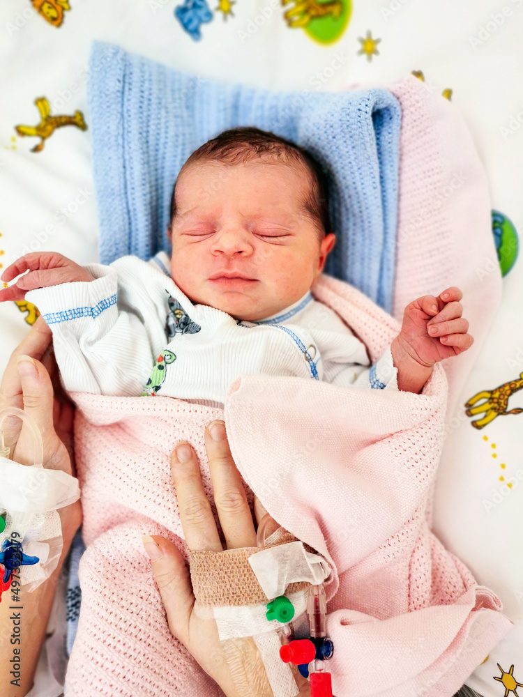 Woman holding her newborn baby with peripheral venous catheter on her