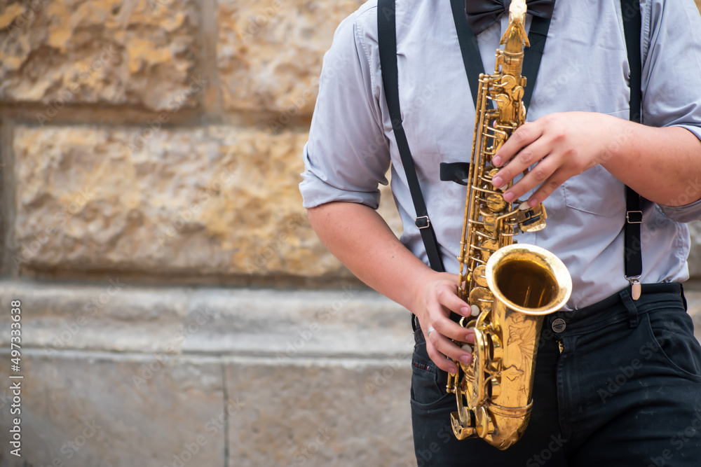 Fototapeta premium Man in a blue T-shirt, suspenders and a tie, playing the saxophone to jazz or blues music on a background with a tattooed background.
