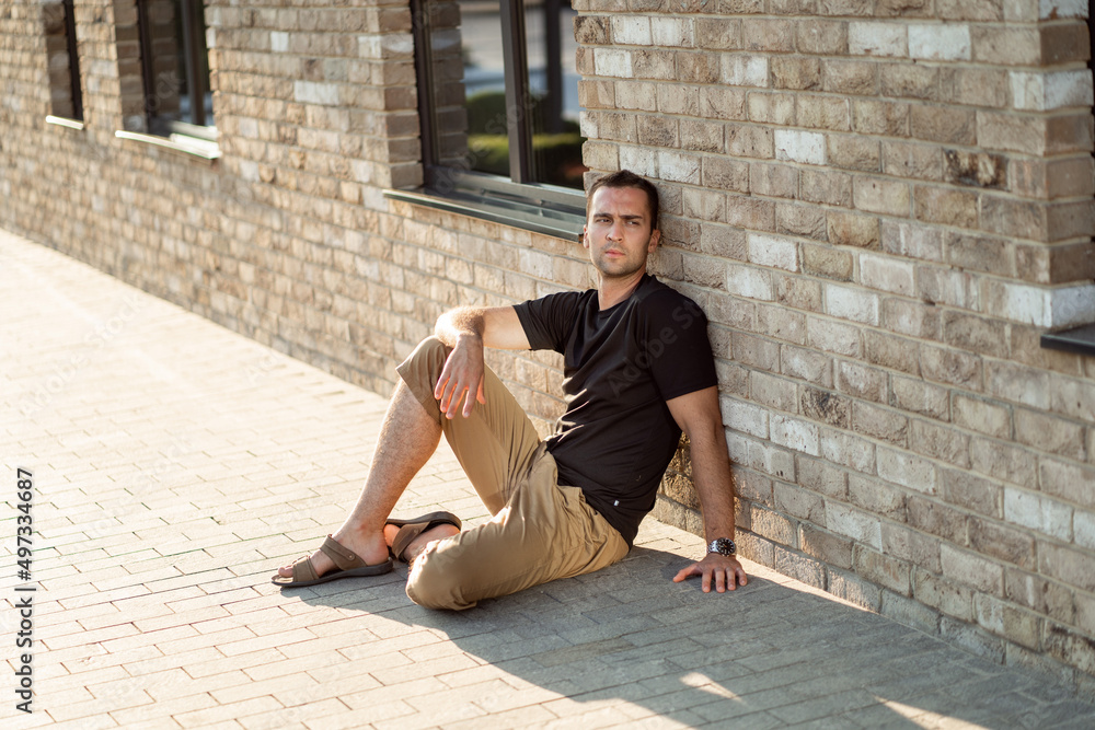 handsome man with short bristles in a black T-shirt on a background of a brick wall sitting on the floor handsome man with short bristles in a black T-shirt on a background of a brick wall sitting on the floor