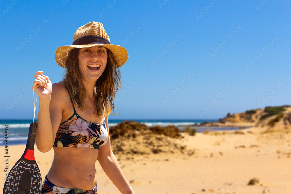 Young woman holding a racket on the seashore smiling at the camera. Summer sport. Copy space. Selective focus.