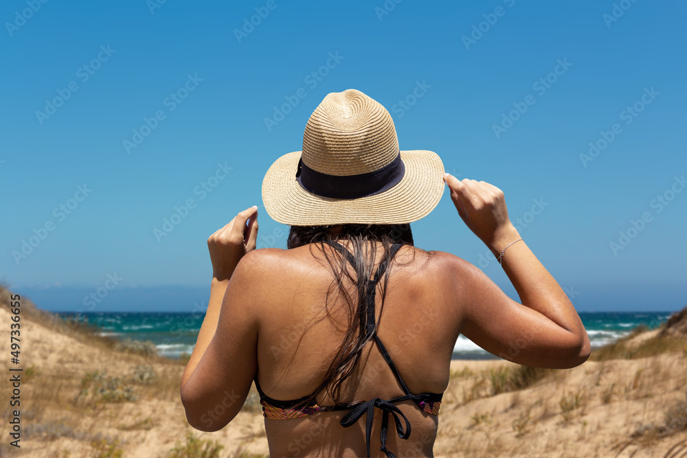 Young woman on her back in bikini with a hat looking at the sea. Copy space. Selective focus.