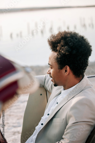 Young black man in nature posing with a convertible. Looking into the distance photo