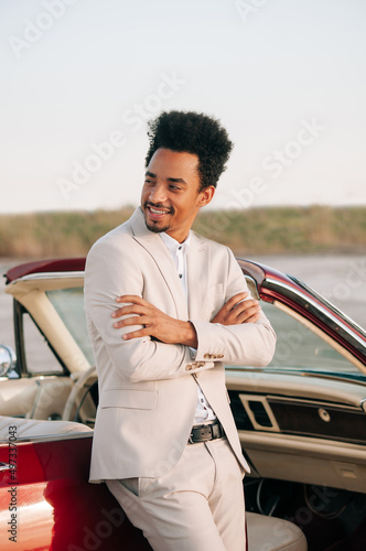 Young black man in nature posing with a convertible. Sunset portrait. photo