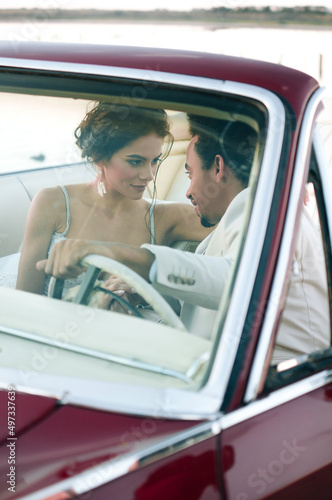 Beautiful couple at sunset on a summer wedding day. Romantic couple in love next to their convertible. The groom is in a light suit, the bride is in a beautiful stylish dress.
