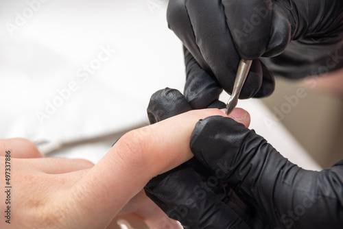 Removal of cuticles on nails. Hands in gloves of a qualified manicurist treating the nails of a young woman with a metal tool, close-up. Hands during a manicure care session in a spa salon.