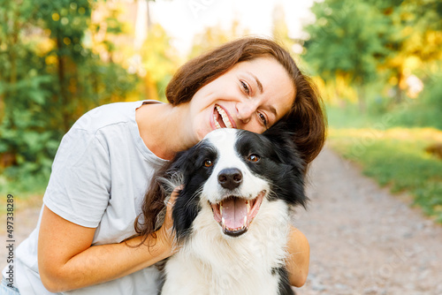 Smiling young attractive woman playing with cute puppy dog border collie on summer outdoor background. Girl holding embracing hugging dog friend. Pet care and animals concept