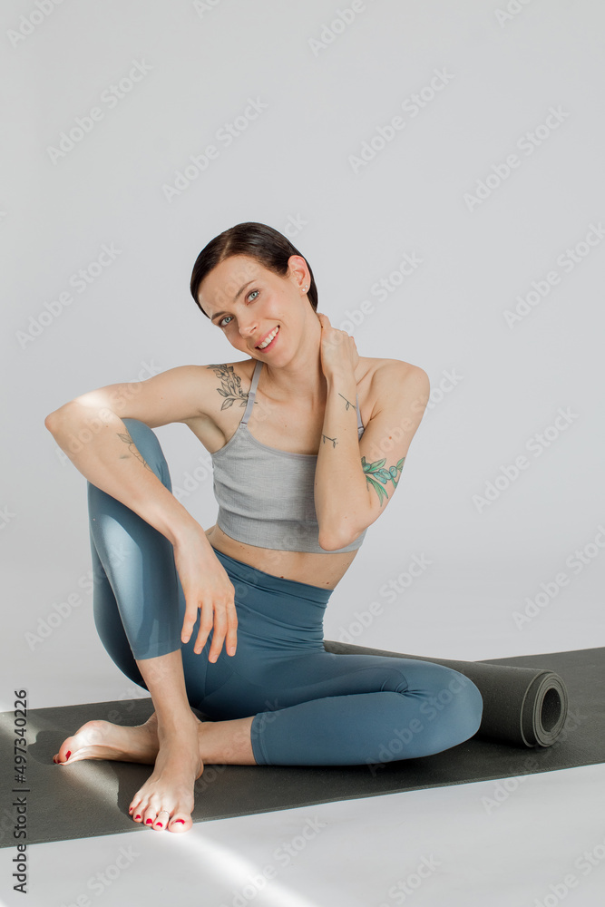 a beautiful girl sits on a rug in a blue-color sportswear. Girl massaging her neck