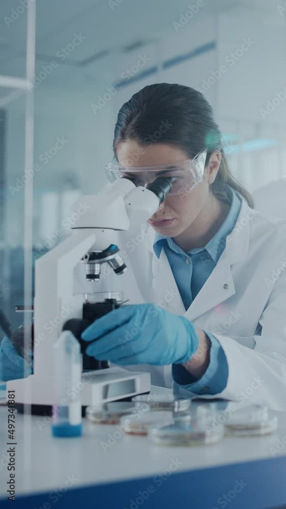 Vertical Video. Medical Development Laboratory: Female Scientist Looking Under Microscope, Analyzing Sample. Specialists Working on Medicine, Biotechnology Research in Advanced Lab. Side View Vertical Video. Medical Development Laboratory: Female Scientist Looking Under Microscope, Analyzing Sample. Specialists Working on Medicine, Biotechnology Research in Advanced Lab. Side View