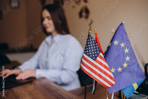 table with two flag usa and eu. A woman is working in the background