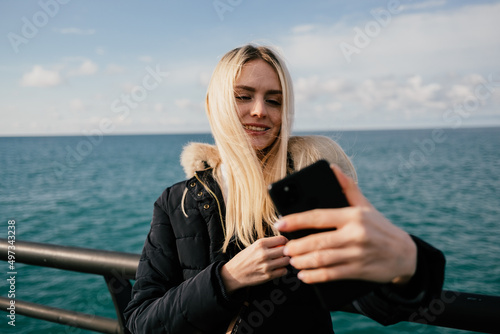 A beautiful smiling blonde girl makes a selfie on the phone against the background of the sea. High quality photo © Екатерина Бучинская