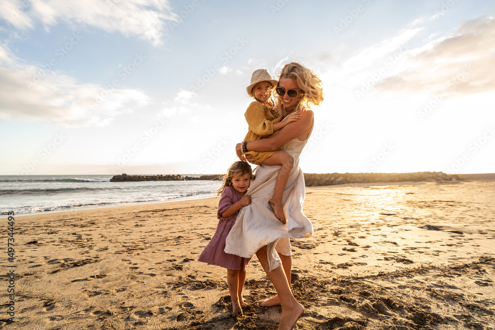Happy beautiful family relaxing and walking at the sunset beach in summer. Smiling mother with her two little daughters having fun on vacations. Happy beautiful family relaxing and walking at the sunset beach in summer. Smiling mother with her two little daughters having fun on vacations.