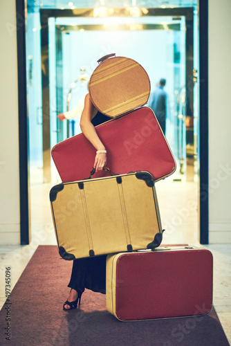 Luckily Ive got all I need. Shot of an unrecognizable young woman carrying a whole bunch of luggage while trying to walk down the lobby of a hotel. photo