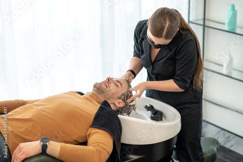 Young man sitting at the chait while having head massage and looking relaxed photo