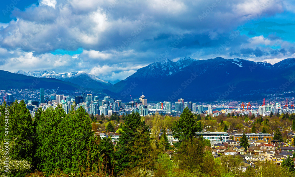 Aerial view of downtown of Vancouver and seaport  with the Rocky Mountains mountain range and stormy sky in the background and cityscape with green trees in the foreground