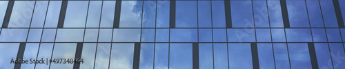 commercial skyscraper wall with design of panoramic windows reflecting blue summer sky and white fluffy clouds