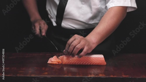 Chef's hand holding fresh piece of salmon.Closeup of chef hands preparing japanese food. Japanese chef making sushi at restaurant.Chef making traditional japanese sushi on wood board.