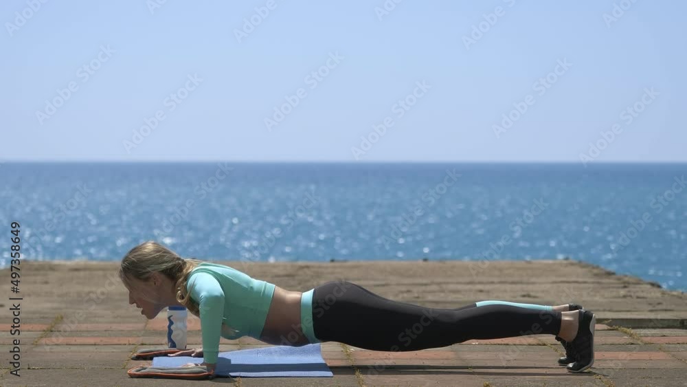 Young blond woman doing push ups near the sea. Fitness healthy lifestyle concept